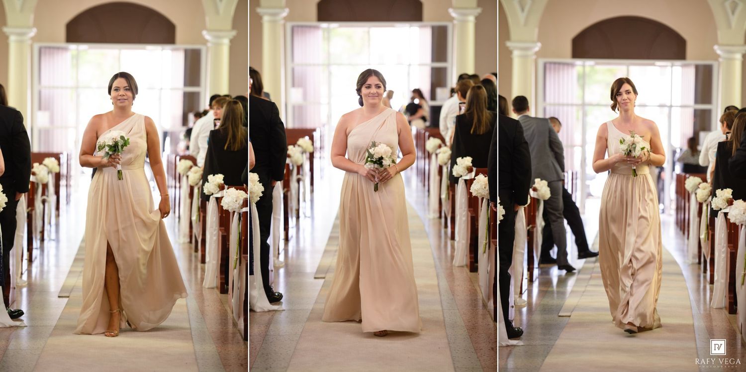 Bridesmaid in champagne gown walks down church aisle holding white bouquet during elegant wedding ceremony.