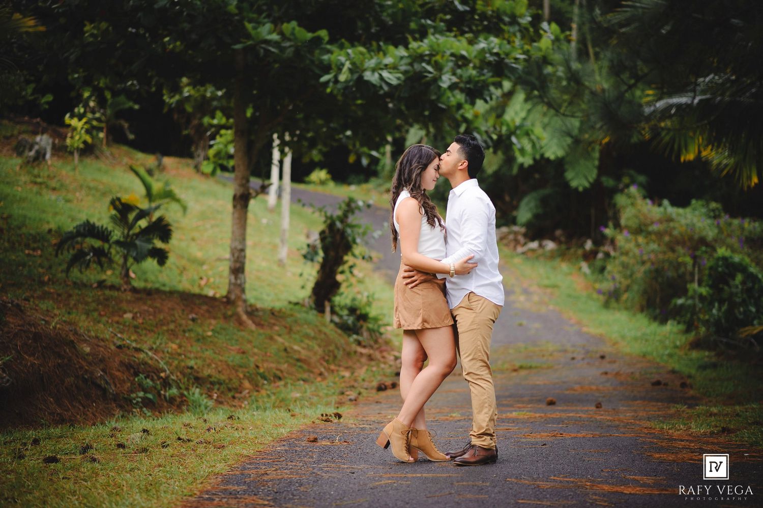 Romantic couple kissing on a scenic countryside road surrounded by tropical greenery.
