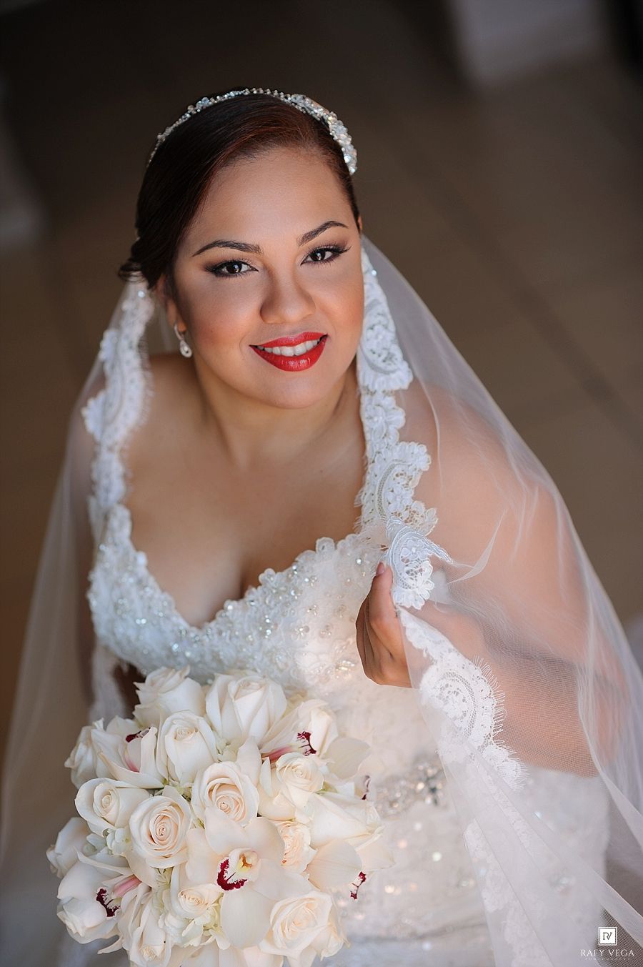 Bride in beaded white dress holding bouquet of white roses and orchids wearing lace veil and tiara.