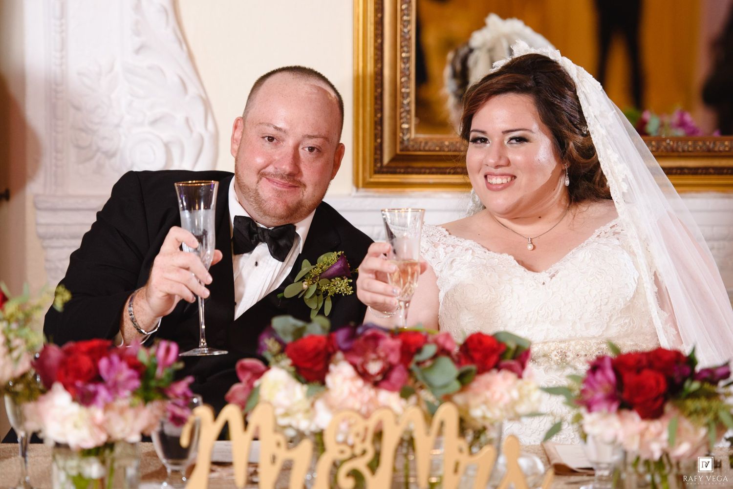 Bride and groom toasting with champagne flutes at Mr. and Mrs. wedding reception sweetheart table.