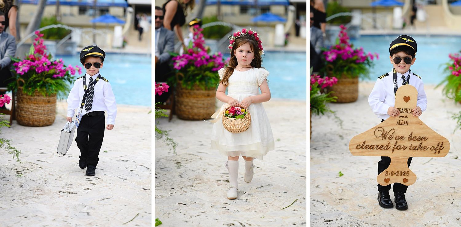 Children dressed as pilots and a flower girl walk down a sandy beach aisle at a tropical wedding.