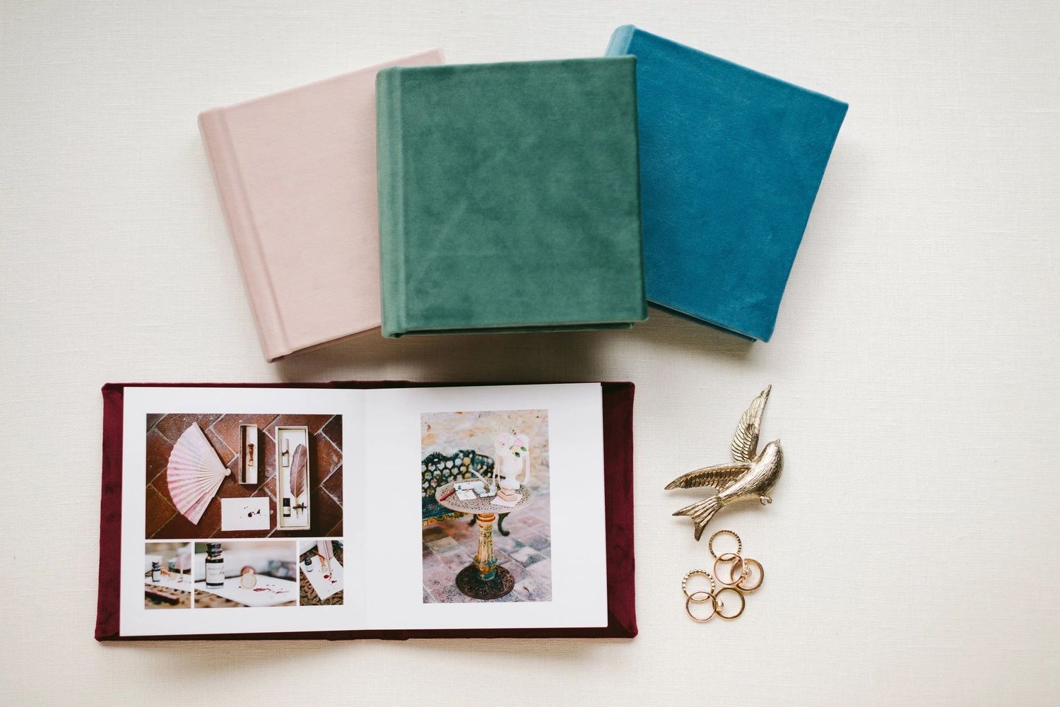 Four velvet photo albums in pink, green, and teal colors displayed with an open burgundy album showing wedding photos.