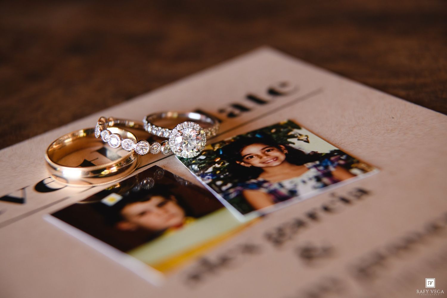 Wedding rings and bands resting on a save-the-date card with a couple's photo on a wooden surface.