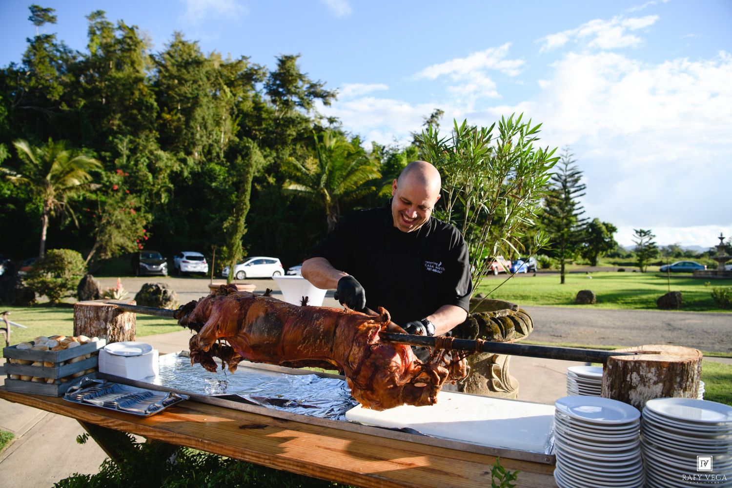 Chef carving a whole roasted pig on a wooden table outdoors at a catering event.