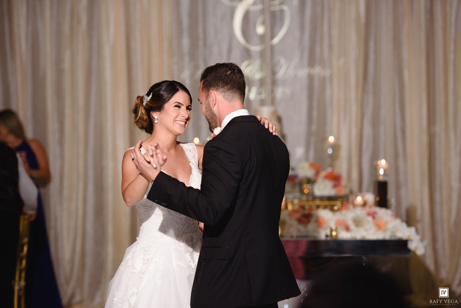 Bride and groom share their first dance at elegant wedding reception with candlelit backdrop and floral arrangements.