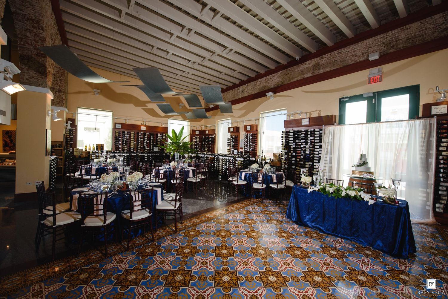 Elegant banquet hall with blue-draped tables, ornate tiled floors, and wine displays for a sophisticated event.