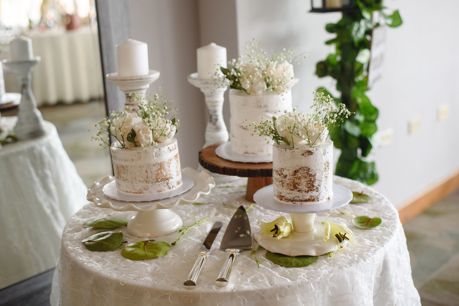 Elegant wedding cake table with three rustic naked cakes adorned with white flowers on a lace-covered table.