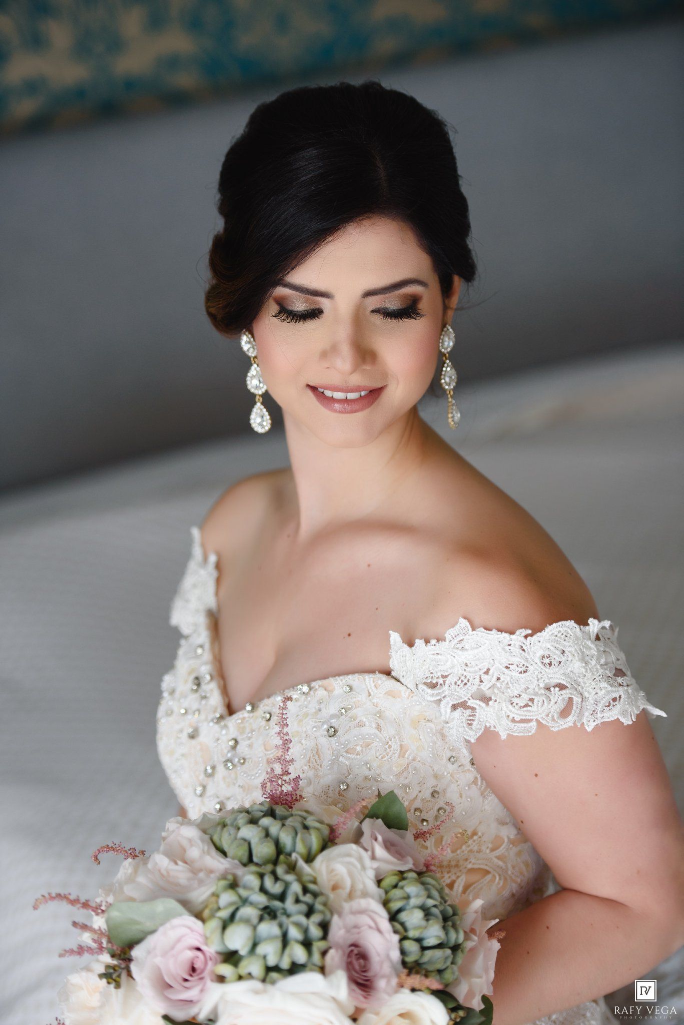 Elegant bride in off-shoulder lace gown holding a bouquet of succulents and pink roses, wearing crystal drop earrings.