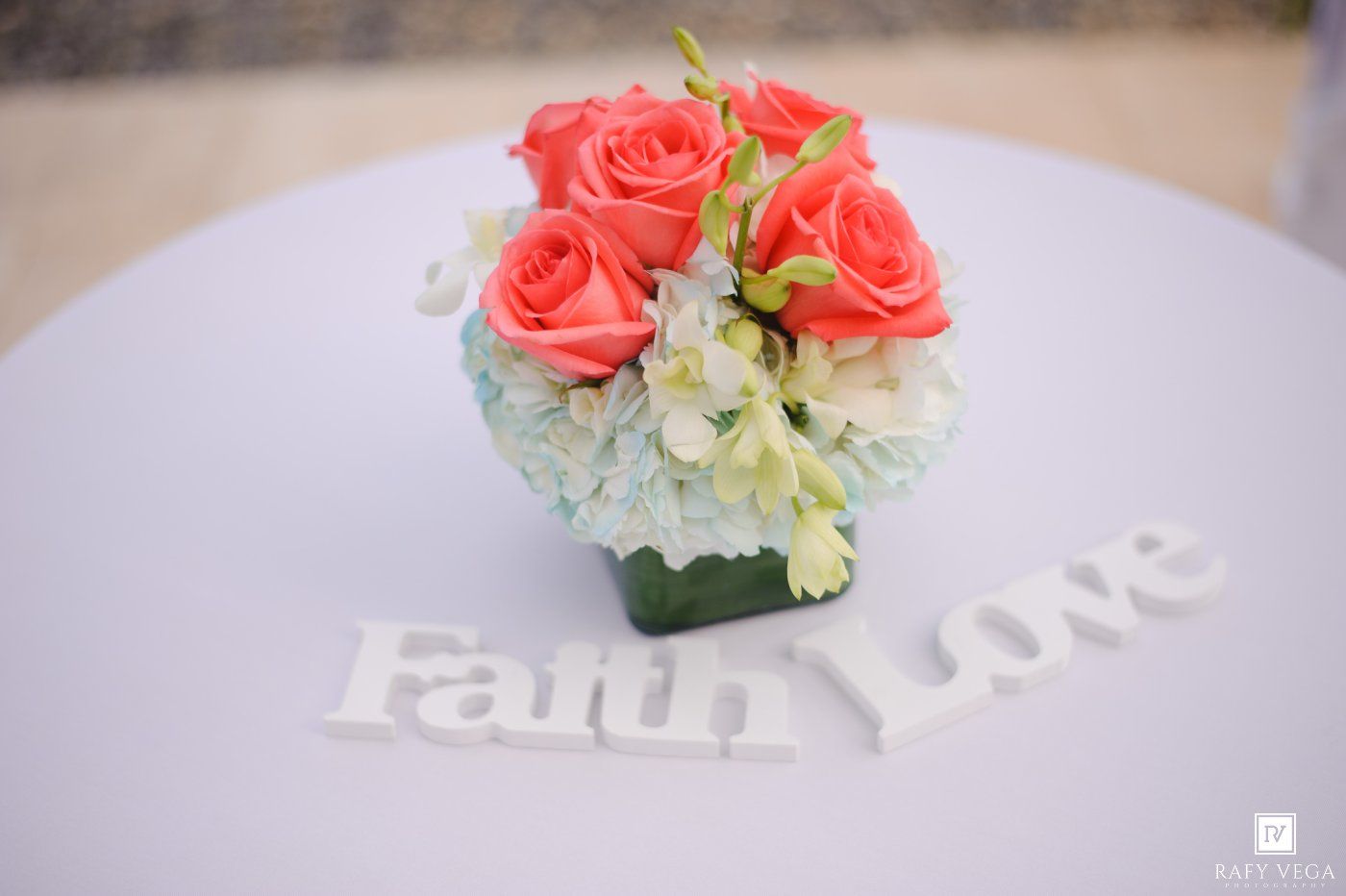 Coral roses and white hydrangeas centerpiece with Faith and Love signs on a white table.