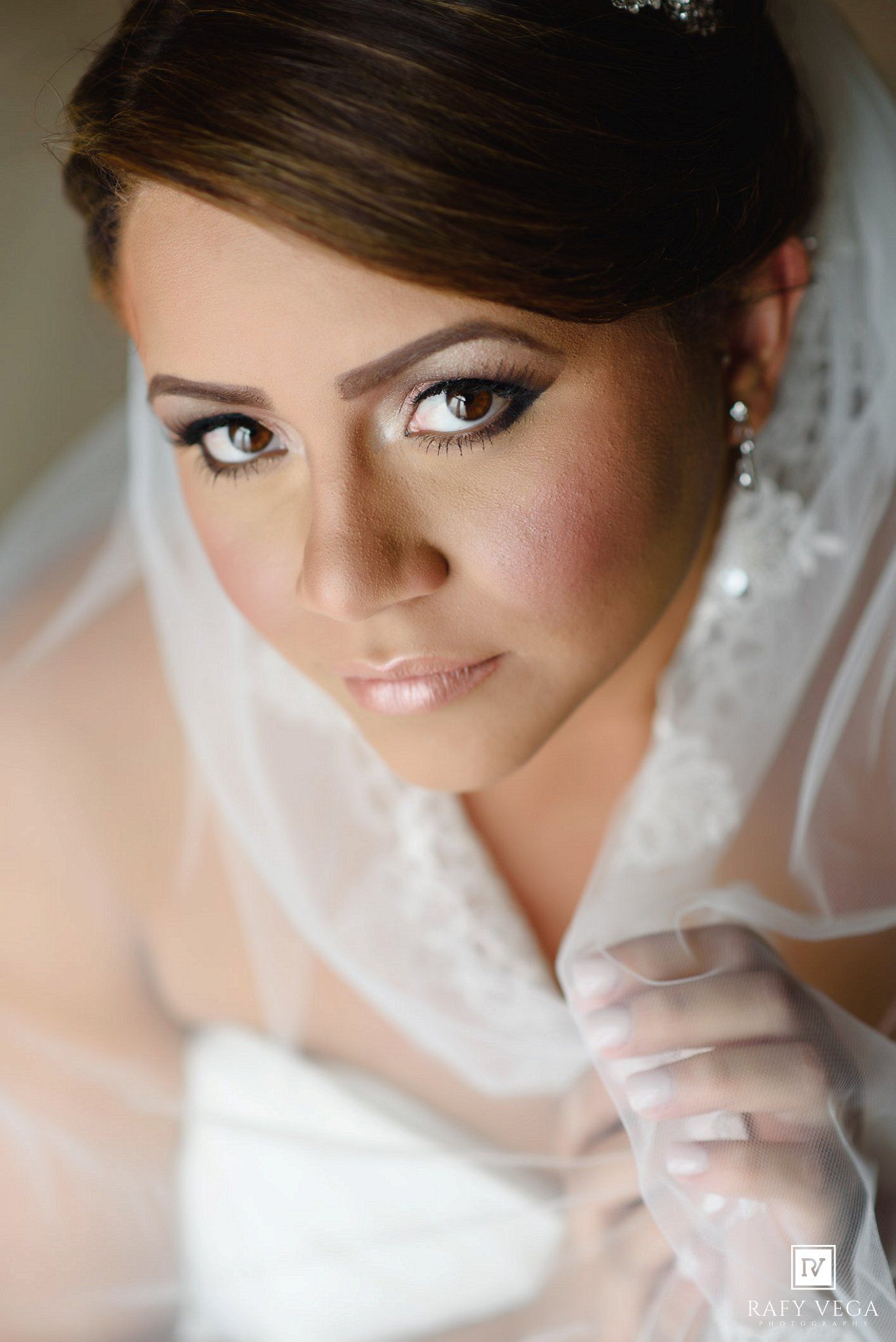 Close-up portrait of a beautiful bride wearing a white veil, lace gown, and elegant makeup on her wedding day.