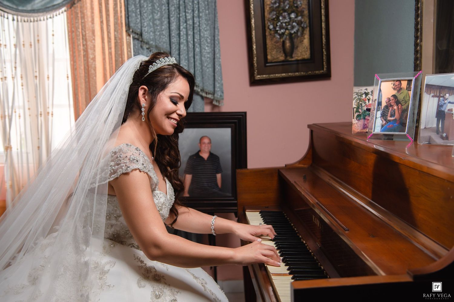 Bride in white wedding gown and veil playing piano, with framed photos displayed on top of the upright piano.