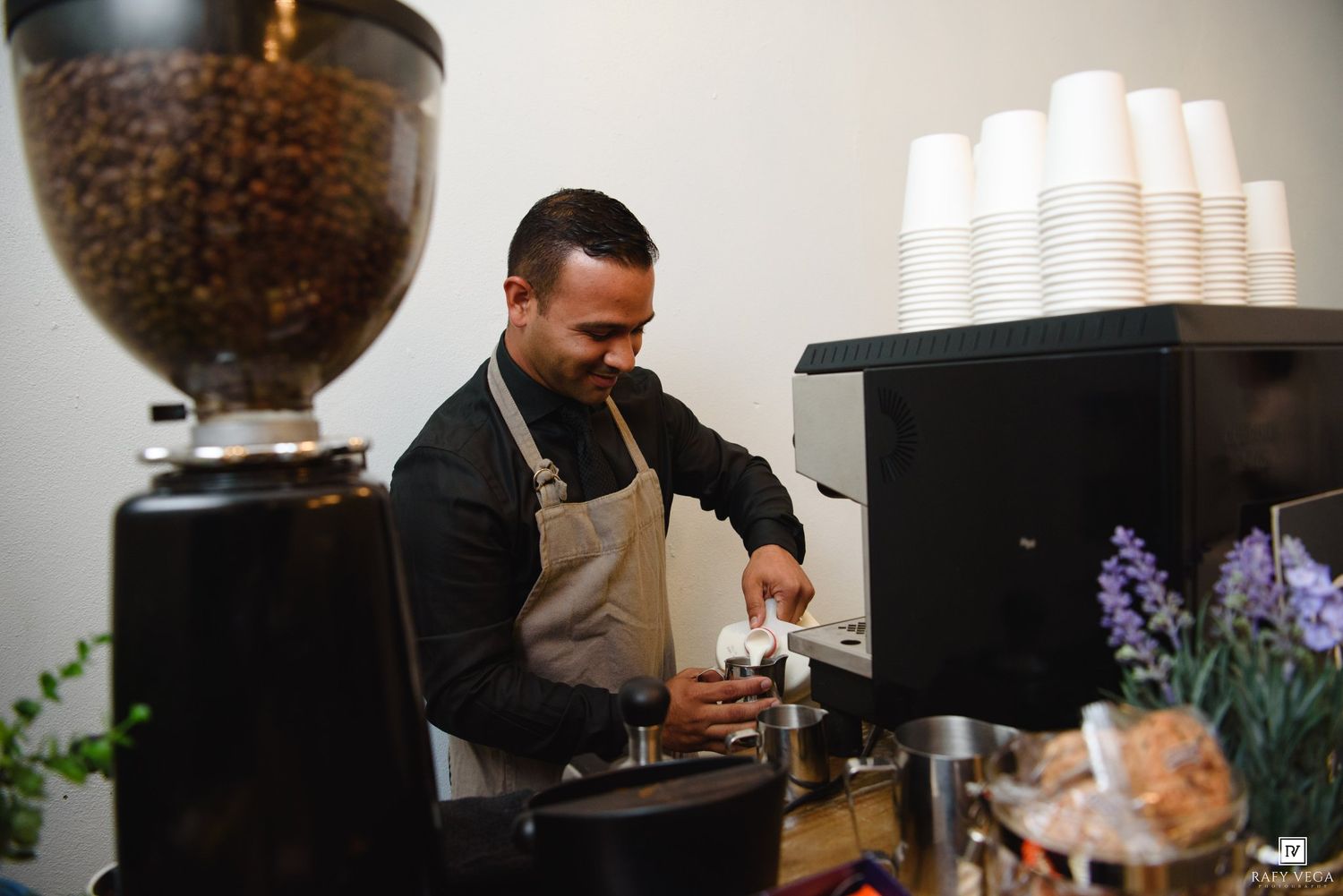 Barista in apron preparing espresso drinks at a professional coffee bar with grinder and cups.