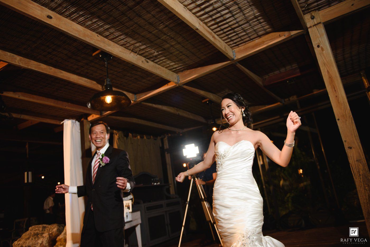 Bride and groom make a grand entrance at their evening wedding reception under rustic wooden beams.