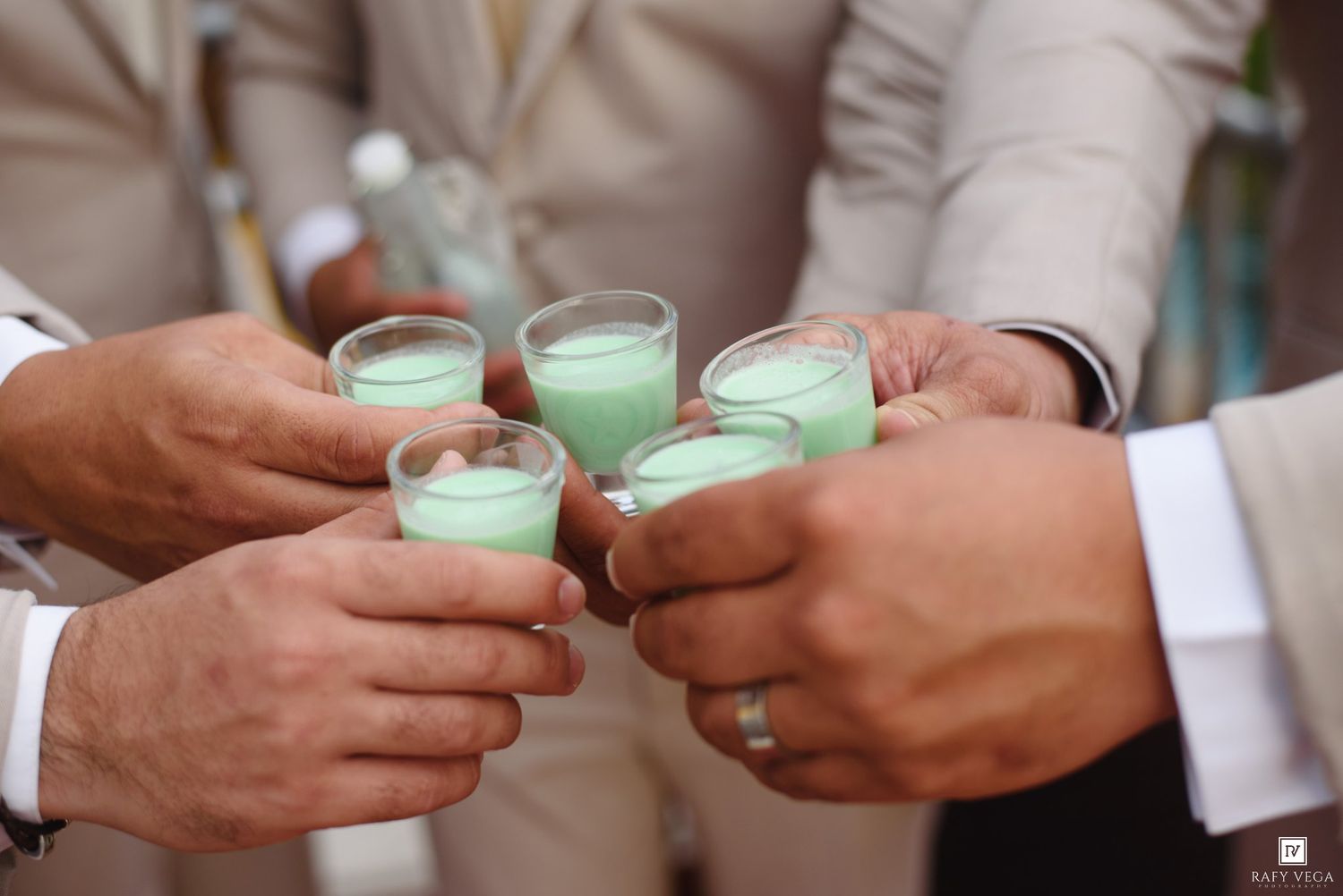Group of men in suits toasting with green shots at a wedding celebration.