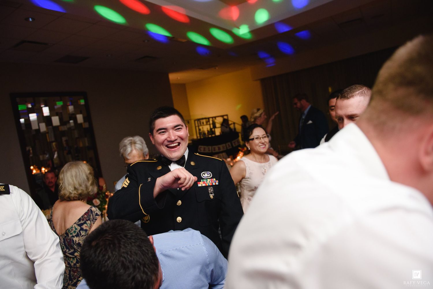 Smiling military officer in uniform dancing joyfully at a colorful wedding reception.