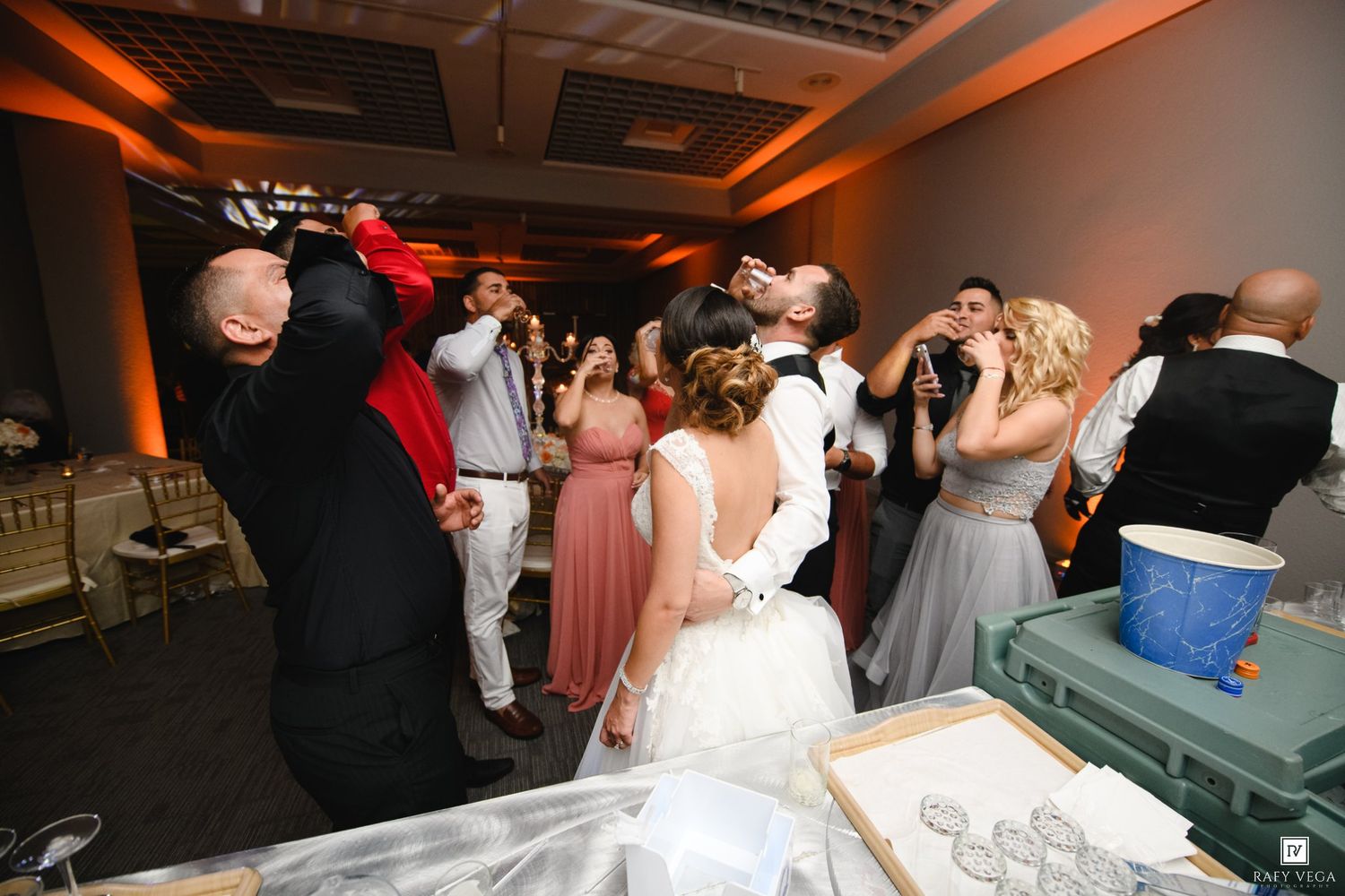 Wedding guests celebrating with bride and groom at lively indoor reception party.