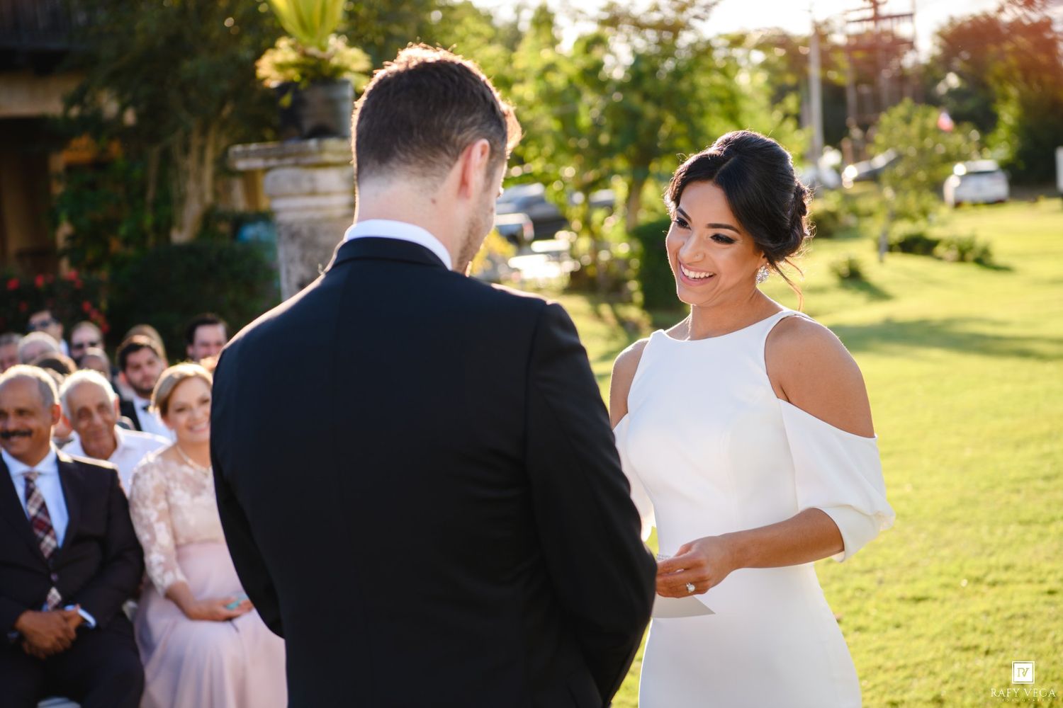 Bride and groom exchanging vows at an outdoor wedding ceremony on a sunny day.