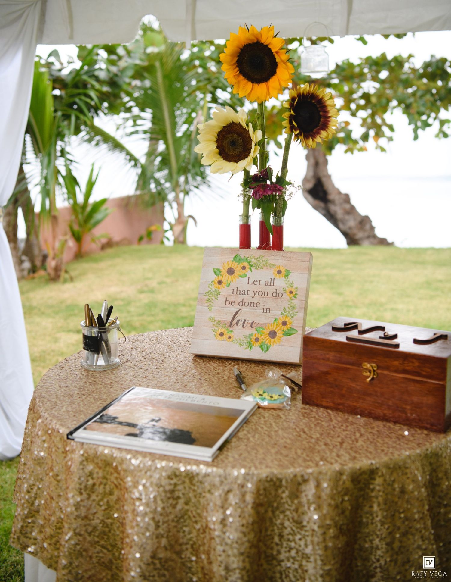 Gold sequin wedding guest book table with sunflowers, wooden box, sign reading Let all that you do be done in love.