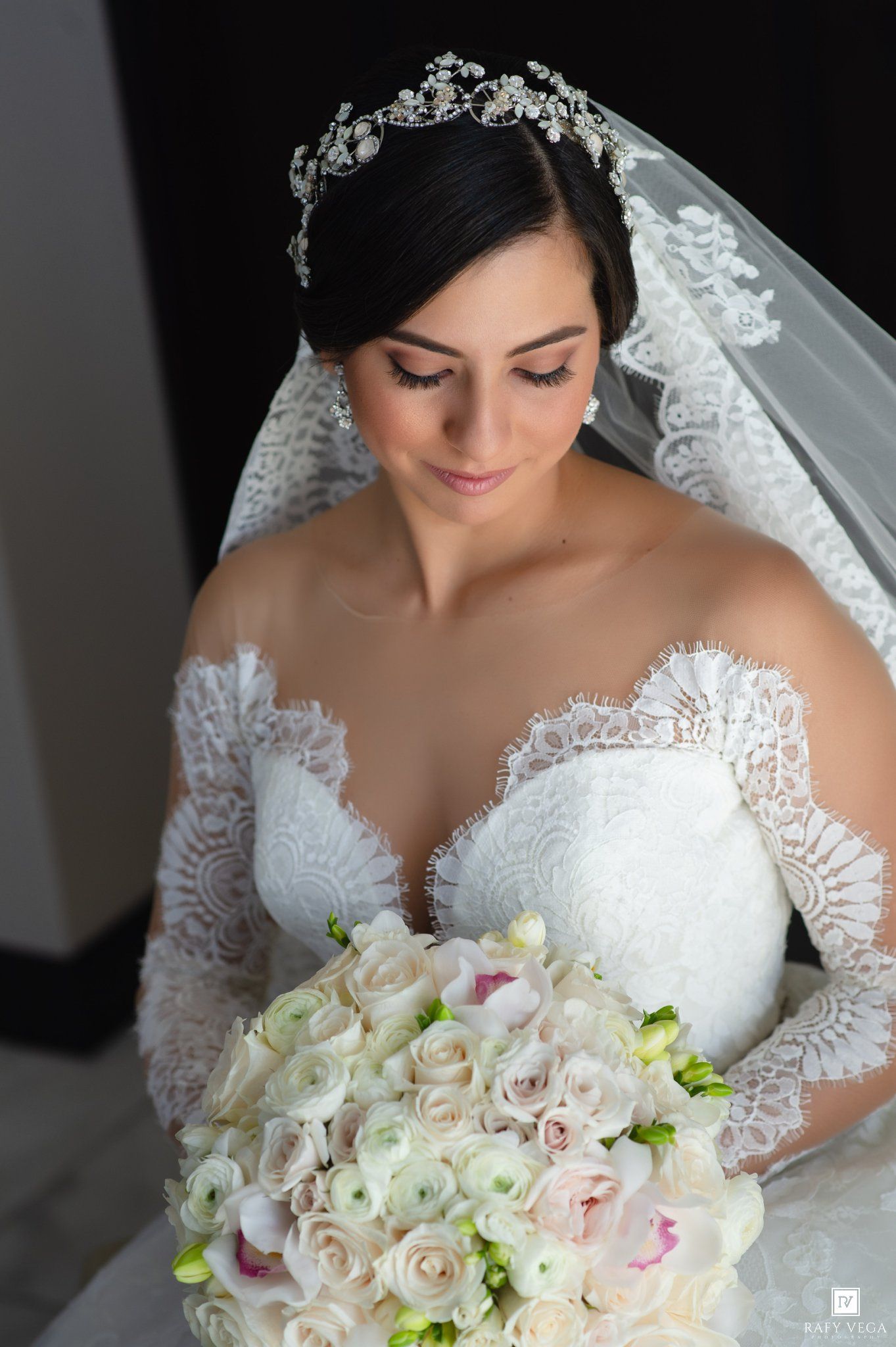Bride in lace wedding gown and crystal tiara holding a bouquet of white and pink roses.