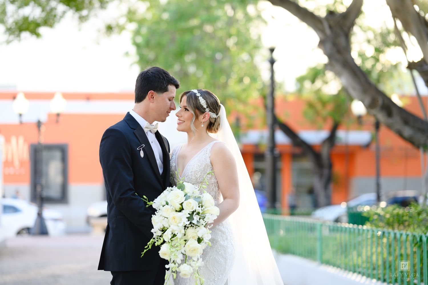 Bride and groom share a romantic moment outdoors, bride holding a white floral bouquet.