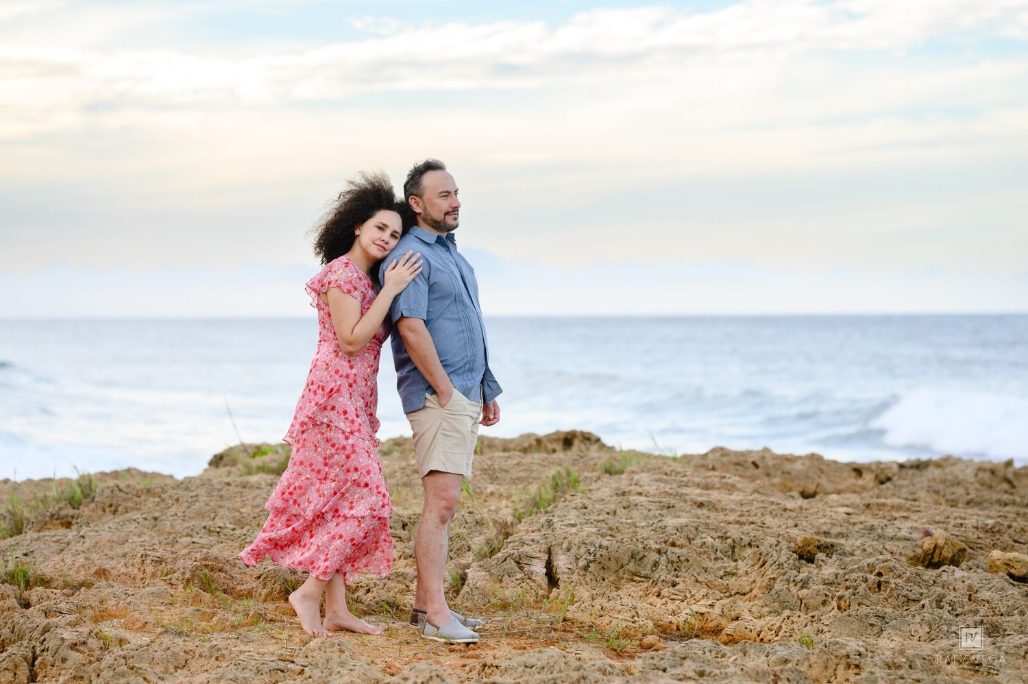 Couple embracing on rocky coastal cliffs with ocean waves in the background at sunset.