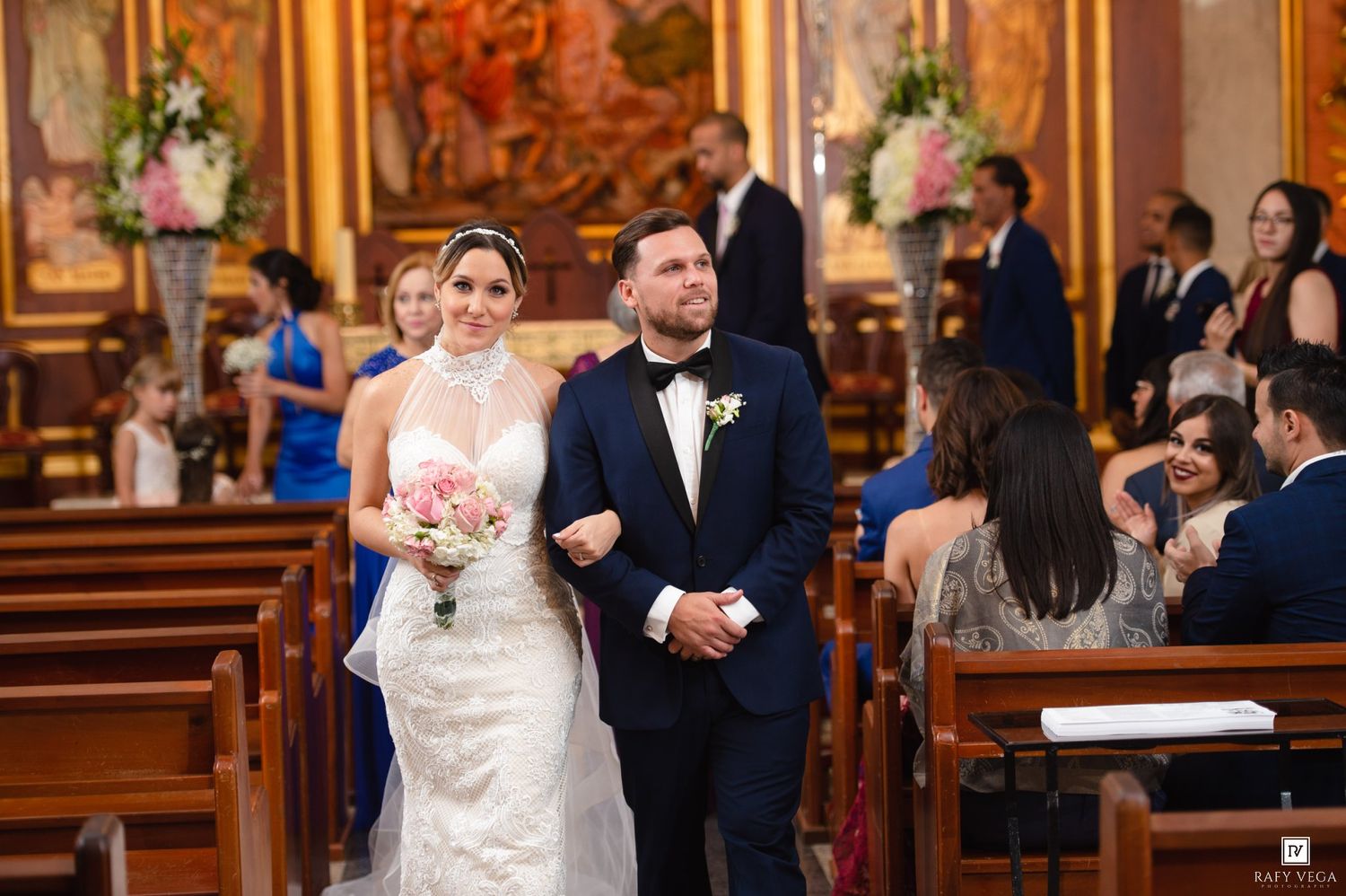 Bride and groom walking down the aisle of an ornate church during a wedding ceremony.