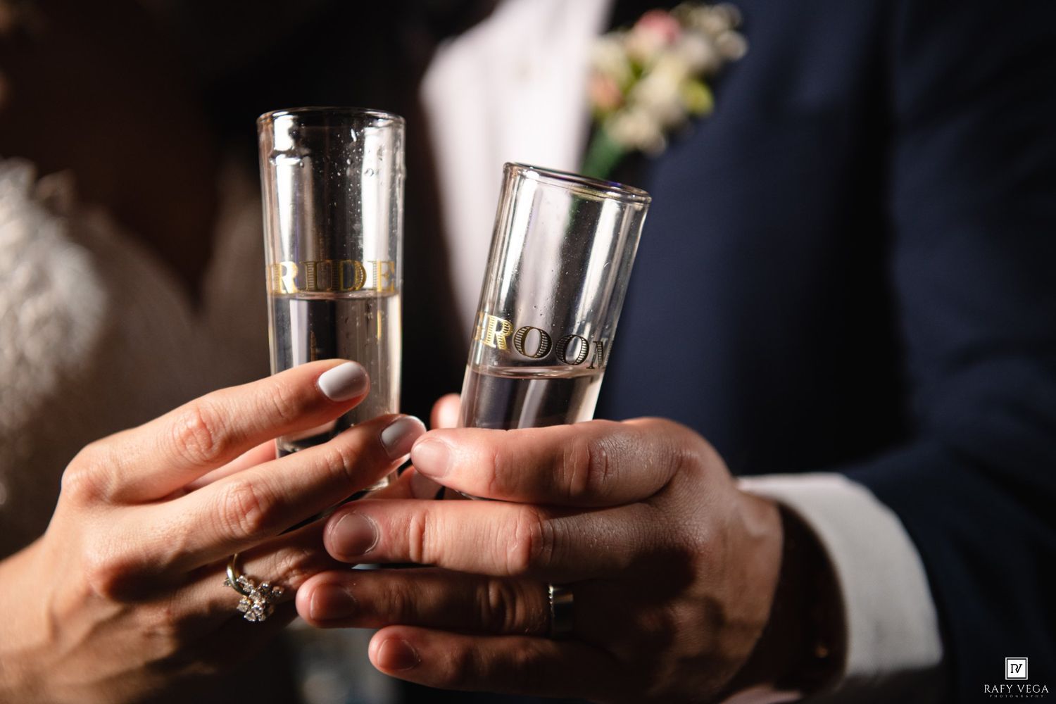 Bride and groom clinking champagne flutes with wedding rings visible, celebrating their marriage toast.