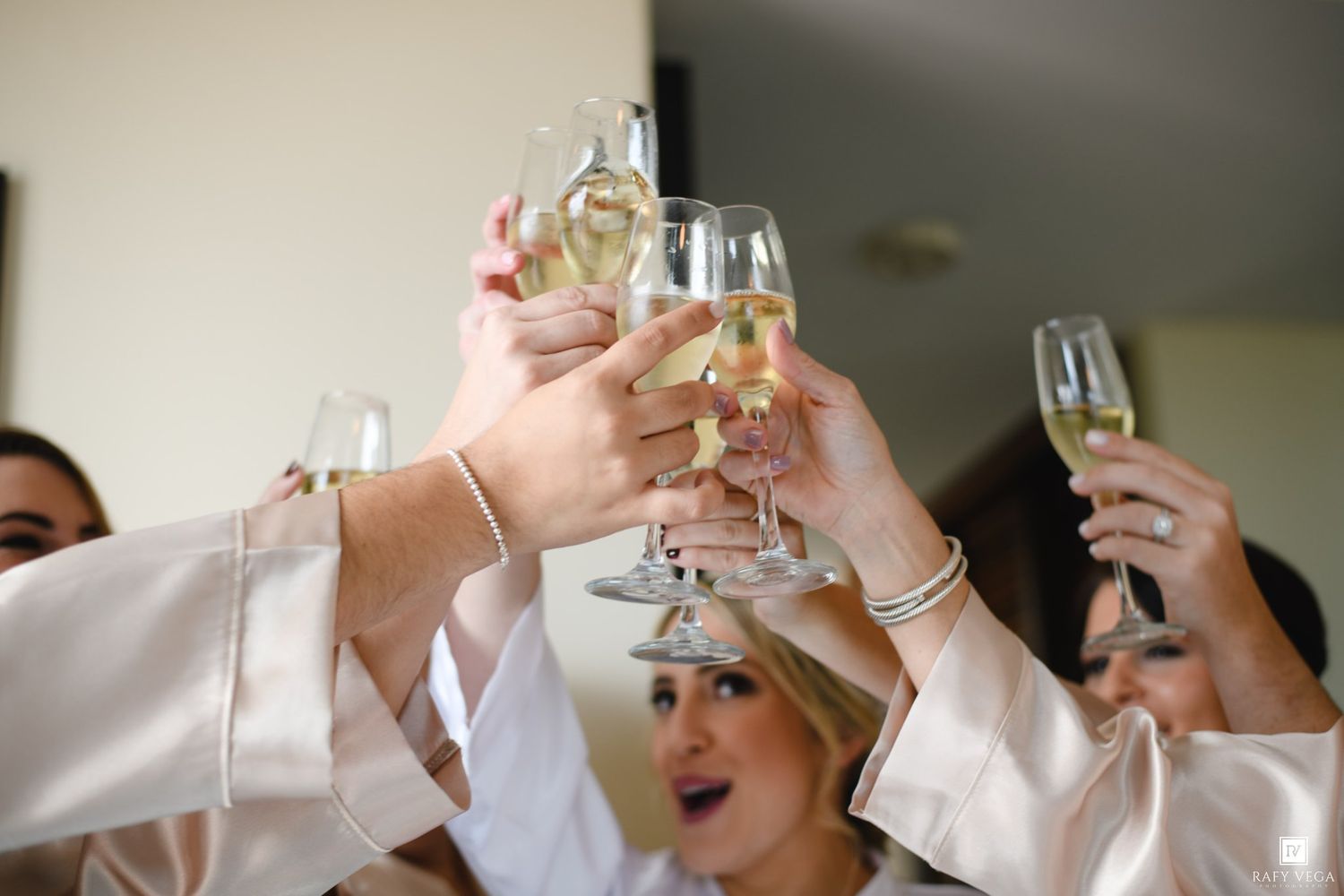 Women in satin robes toasting with champagne glasses at a bridal party celebration.