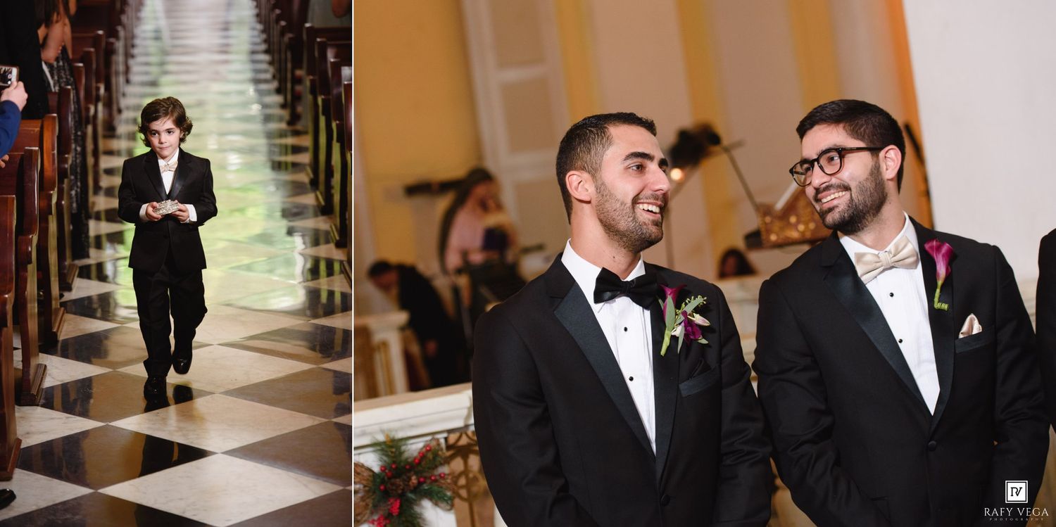 Two grooms in tuxedos smile at their wedding ceremony as a guest walks down the aisle in a black suit.