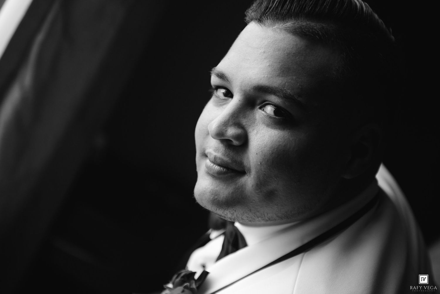 Black and white portrait of a young man smiling softly, wearing a white shirt, captured in elegant studio lighting.