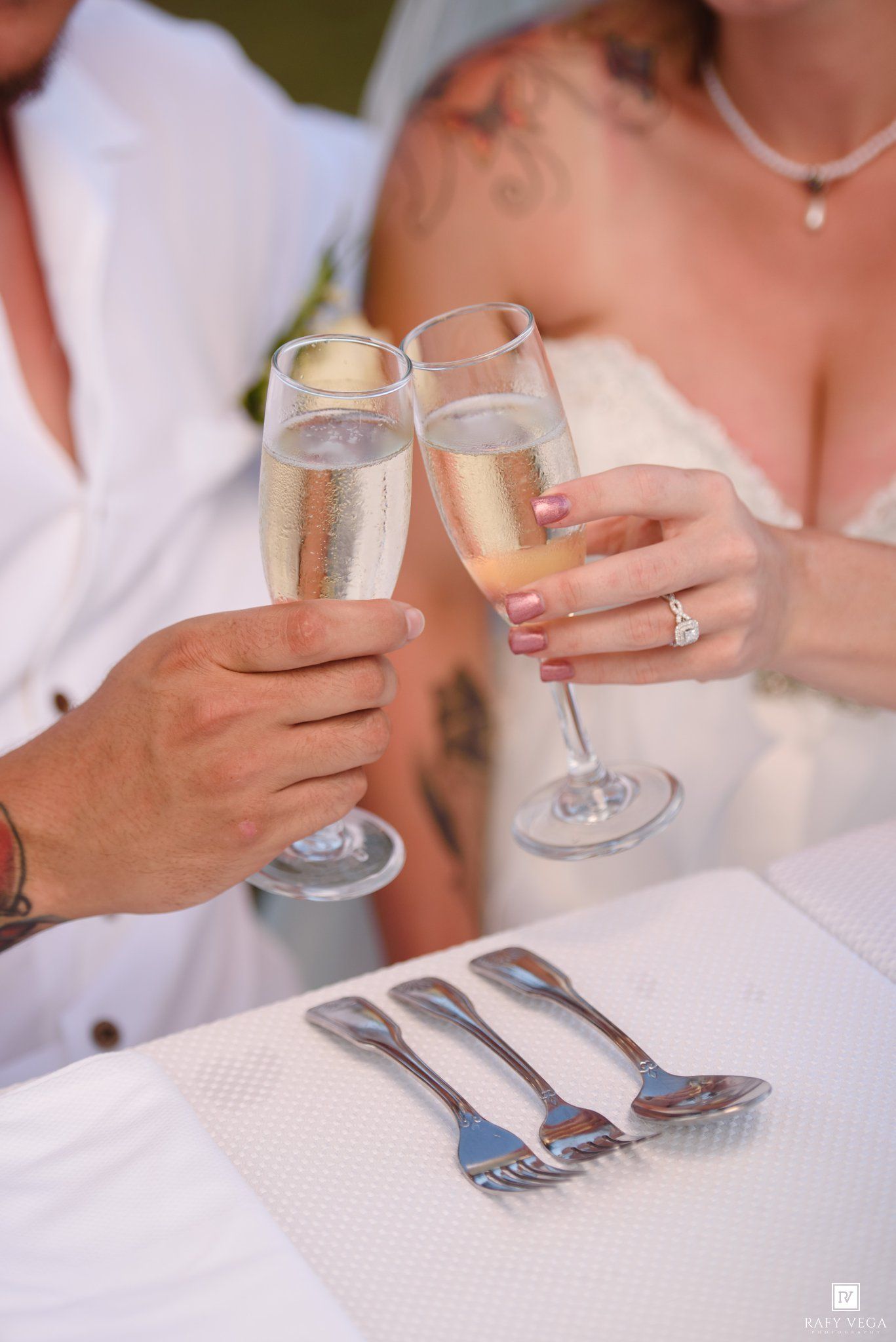 Bride and groom toasting with champagne flutes at wedding reception table with silverware.