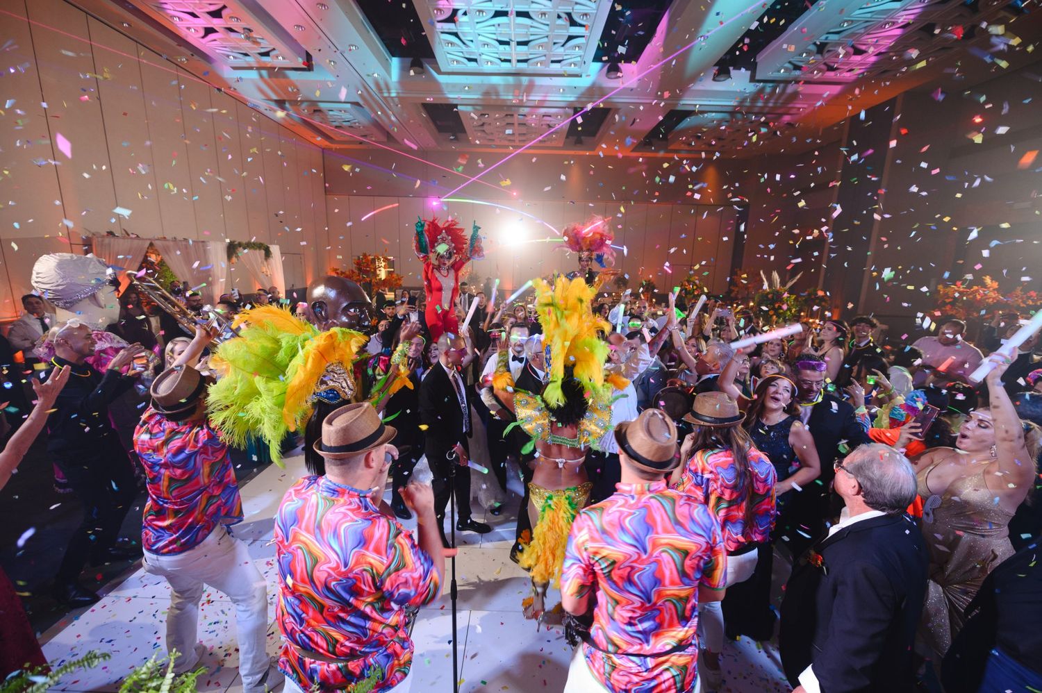 Colorful carnival party with confetti, feathered costumes, and crowd dancing in a festive ballroom celebration.