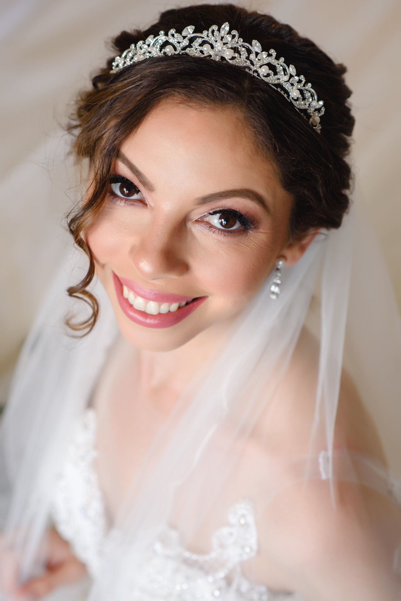 Smiling bride wearing a crystal tiara and white veil with lace wedding dress, elegant bridal makeup and updo hairstyle.