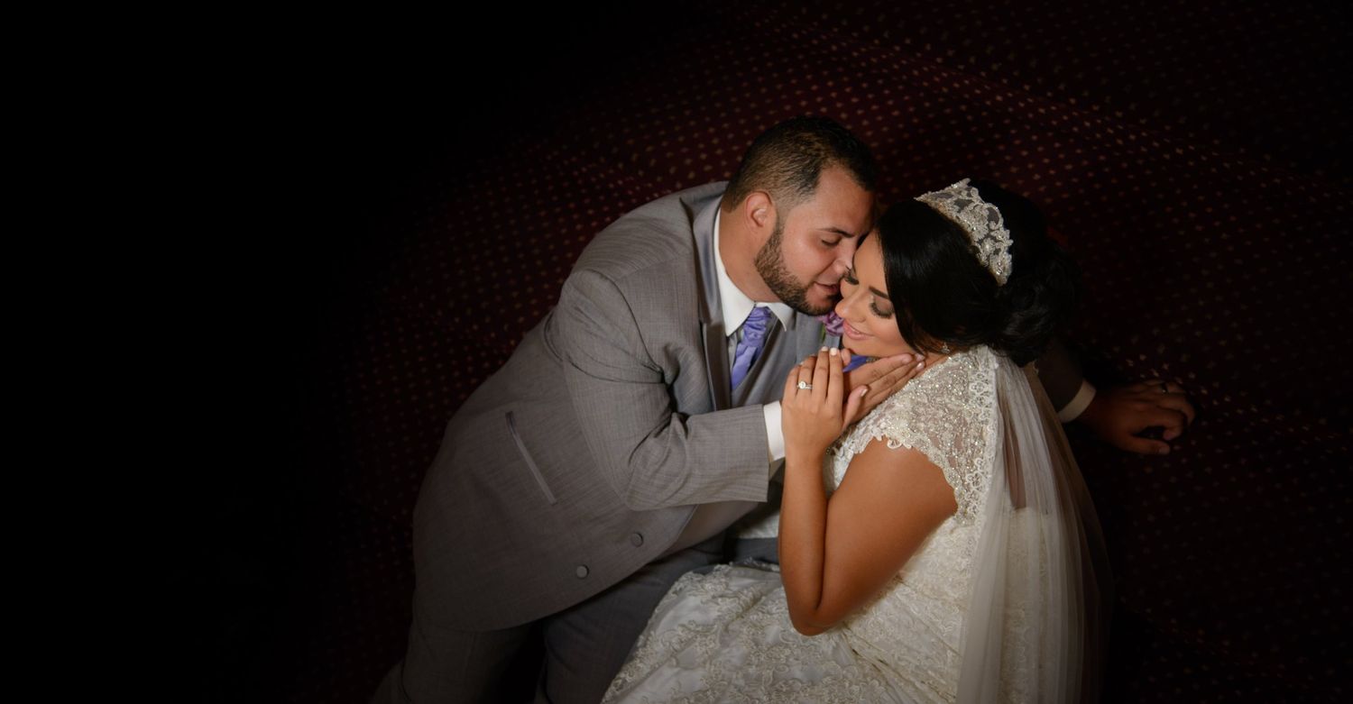 Bride and groom sharing a romantic kiss, bride wearing a white gown and tiara, groom in a gray suit.