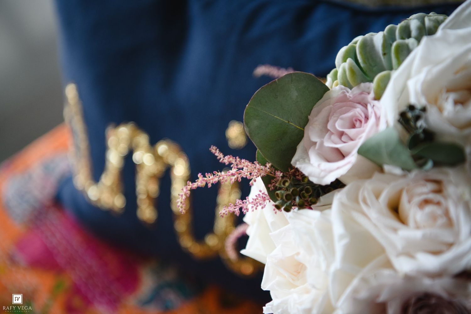 Close-up of a bridal bouquet with blush roses and succulents beside a navy blue Mrs. embroidered wedding bag.