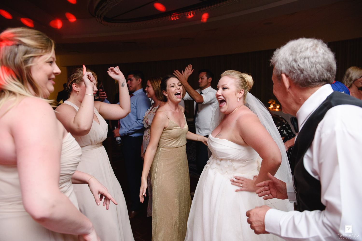 Bride laughs and dances with bridesmaids on wedding reception dance floor.