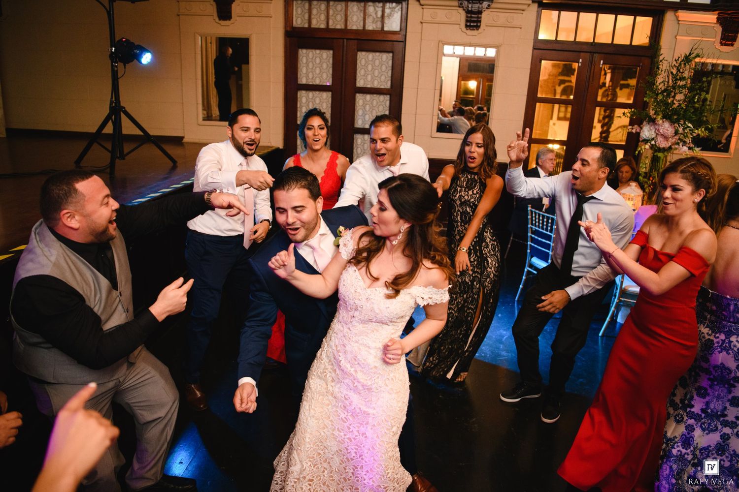Bride and groom dance joyfully surrounded by guests in formal attire at a lively wedding reception.