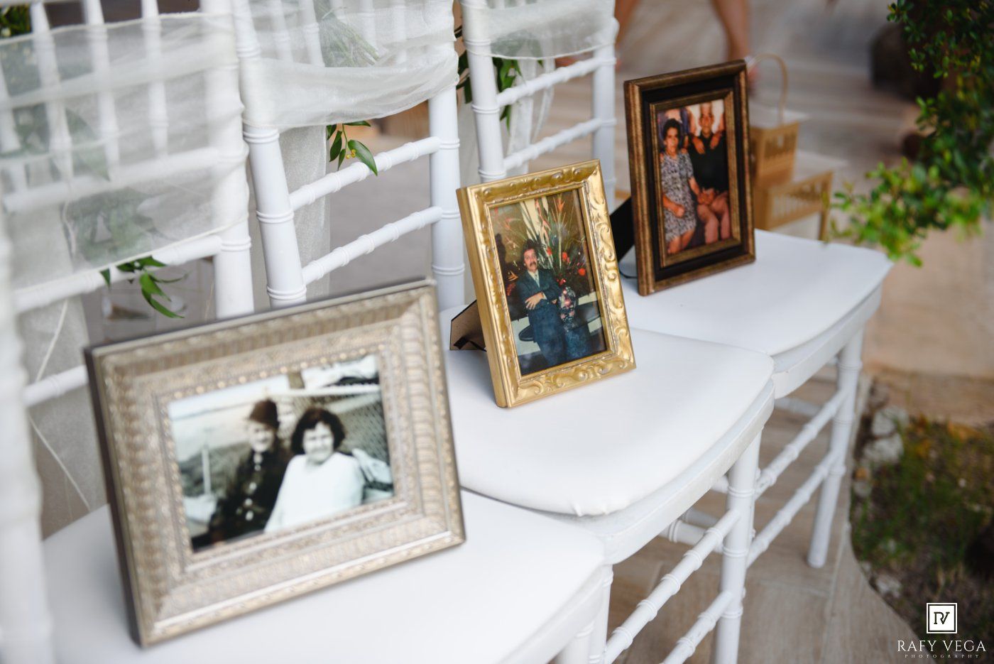 Three vintage framed family photos displayed on a white chair at an outdoor wedding ceremony.