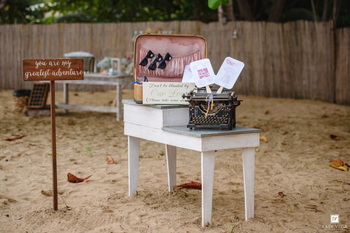Vintage wedding decor with typewriter and suitcase on white table on sandy beach.