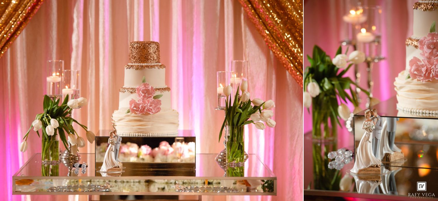Elegant wedding cake display with white and pink floral decorations, candles, and tulip arrangements on a mirrored table.