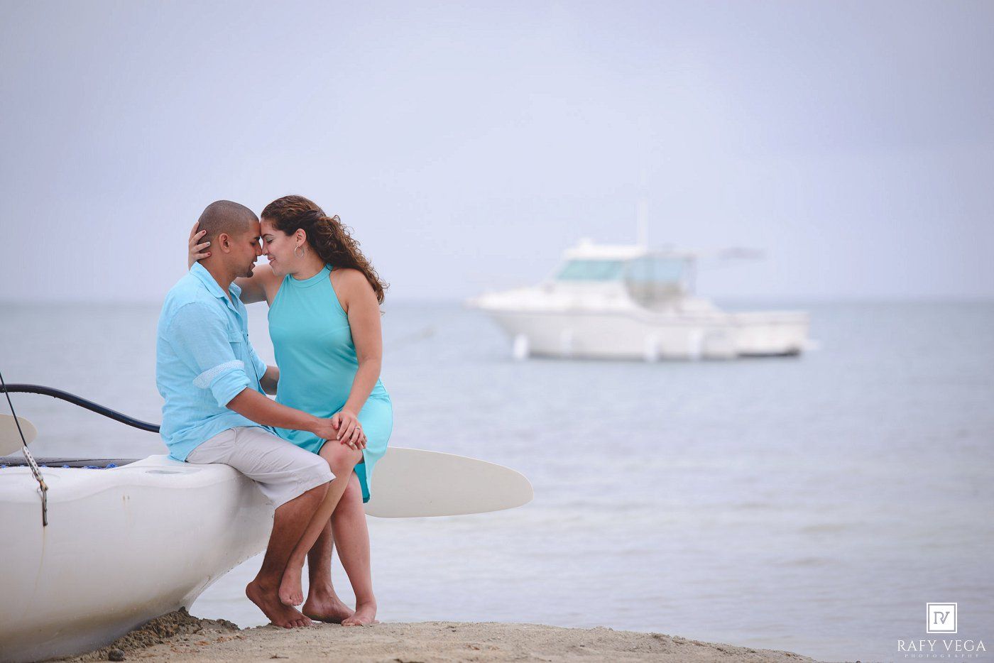 A romantic couple shares an intimate moment sitting on a boat on a calm tropical beach.