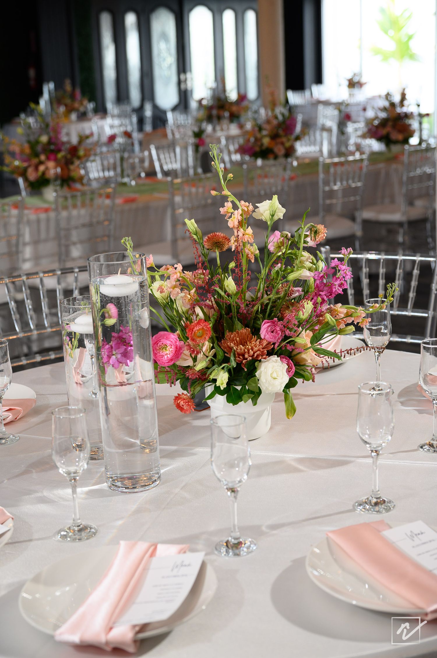Elegant wedding reception table with pink and coral floral centerpiece, floating candle vase, wine glasses and blush napkins.