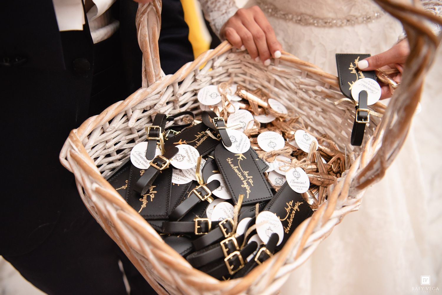 Wicker basket filled with black and gold wedding favor keychains held by bride and groom.
