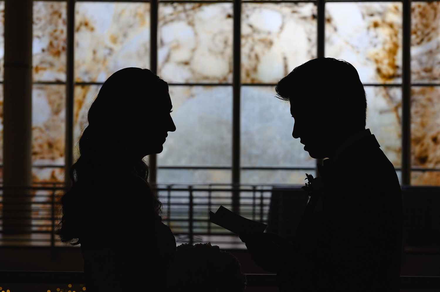 Silhouettes of two people facing each other in conversation against a backlit ornate window background.