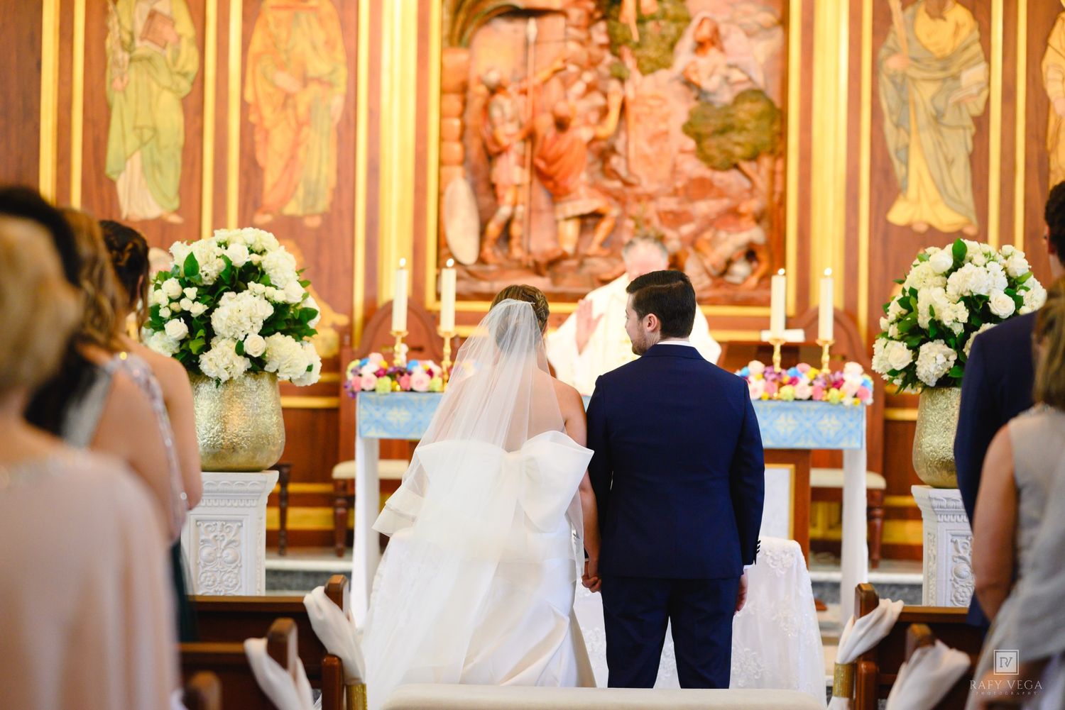 Bride and groom stand at church altar during wedding ceremony with floral arrangements and religious artwork.