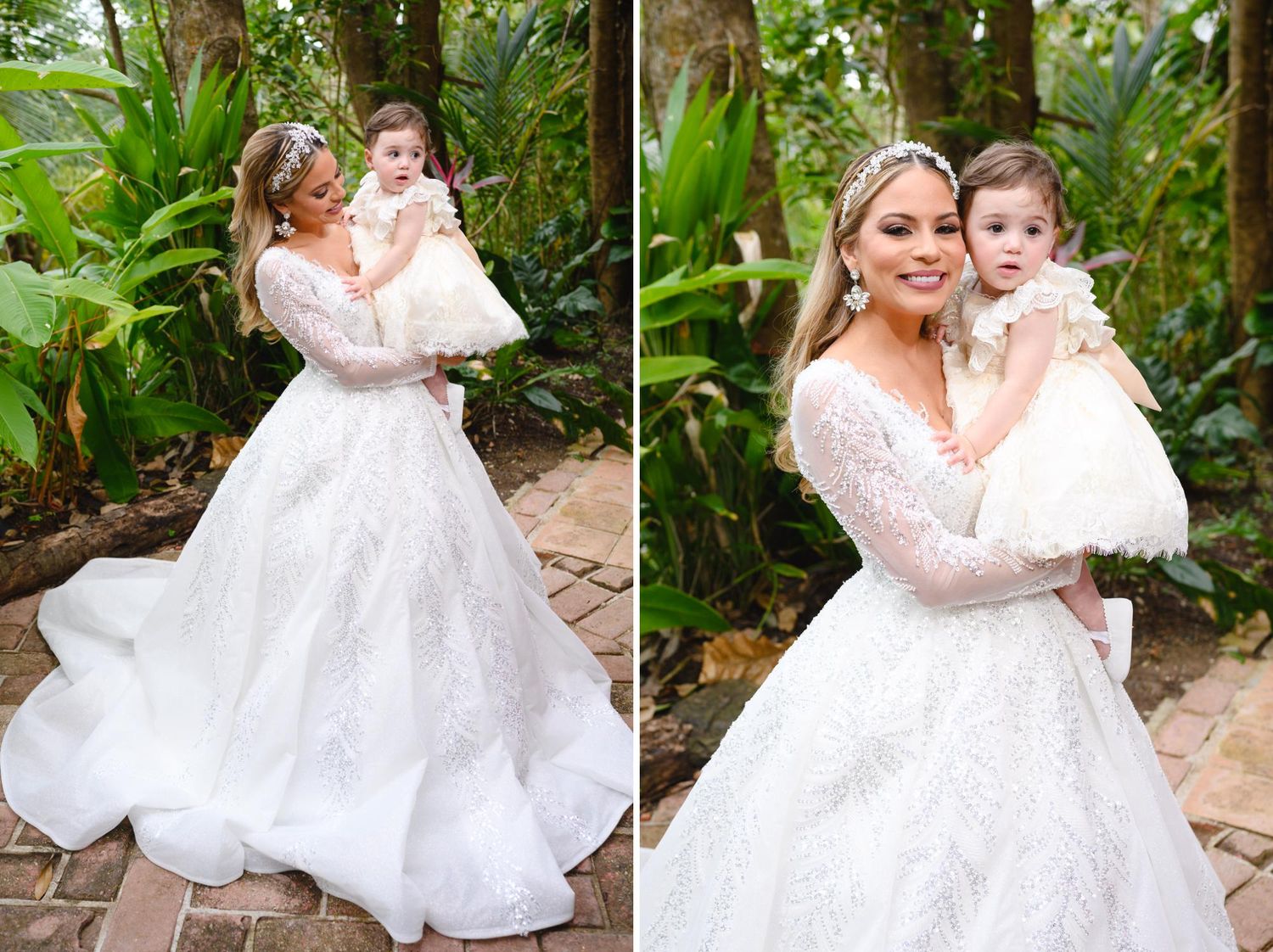 Bride in a long-sleeve lace ball gown holding a baby in white dress outdoors among lush greenery.