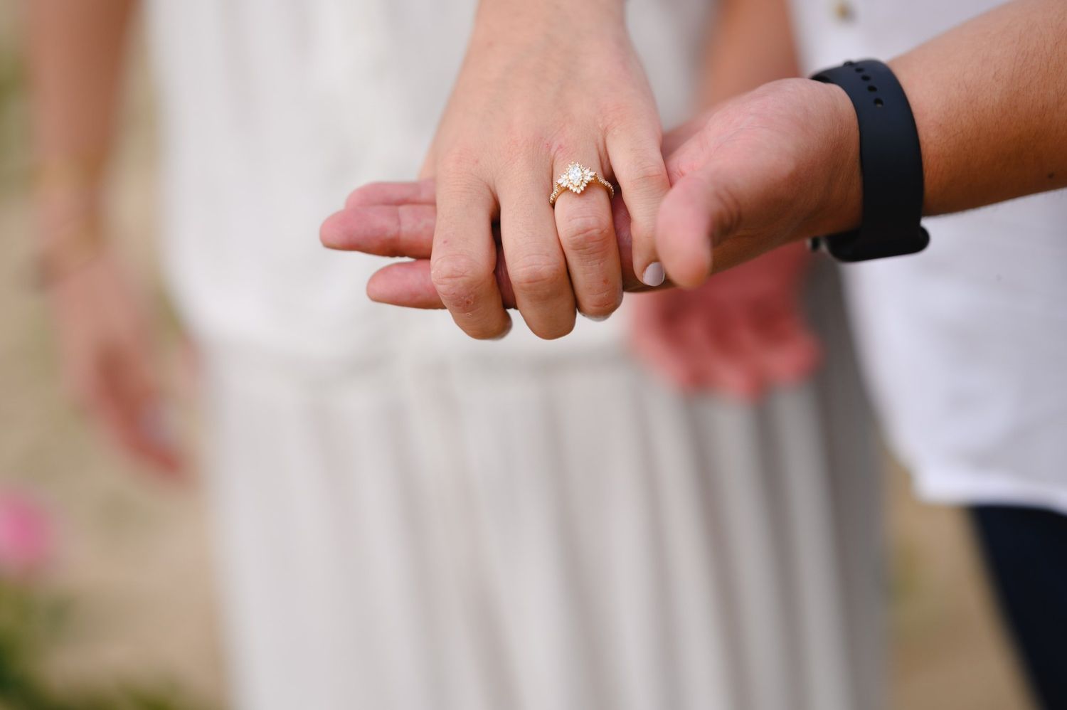 Couple holding hands showing engagement ring and fitness tracker, romantic outdoor wedding photo.