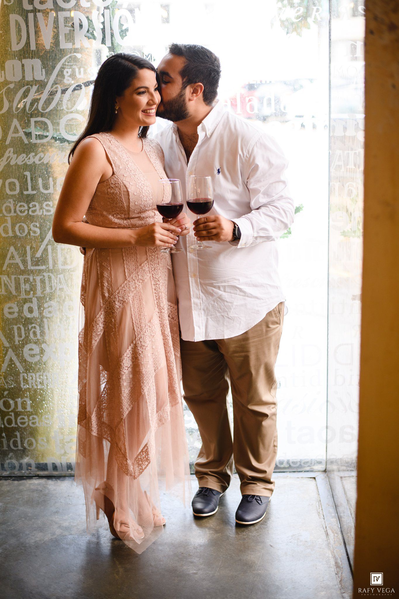 Romantic couple sharing a tender moment with red wine glasses in a warmly lit restaurant setting.