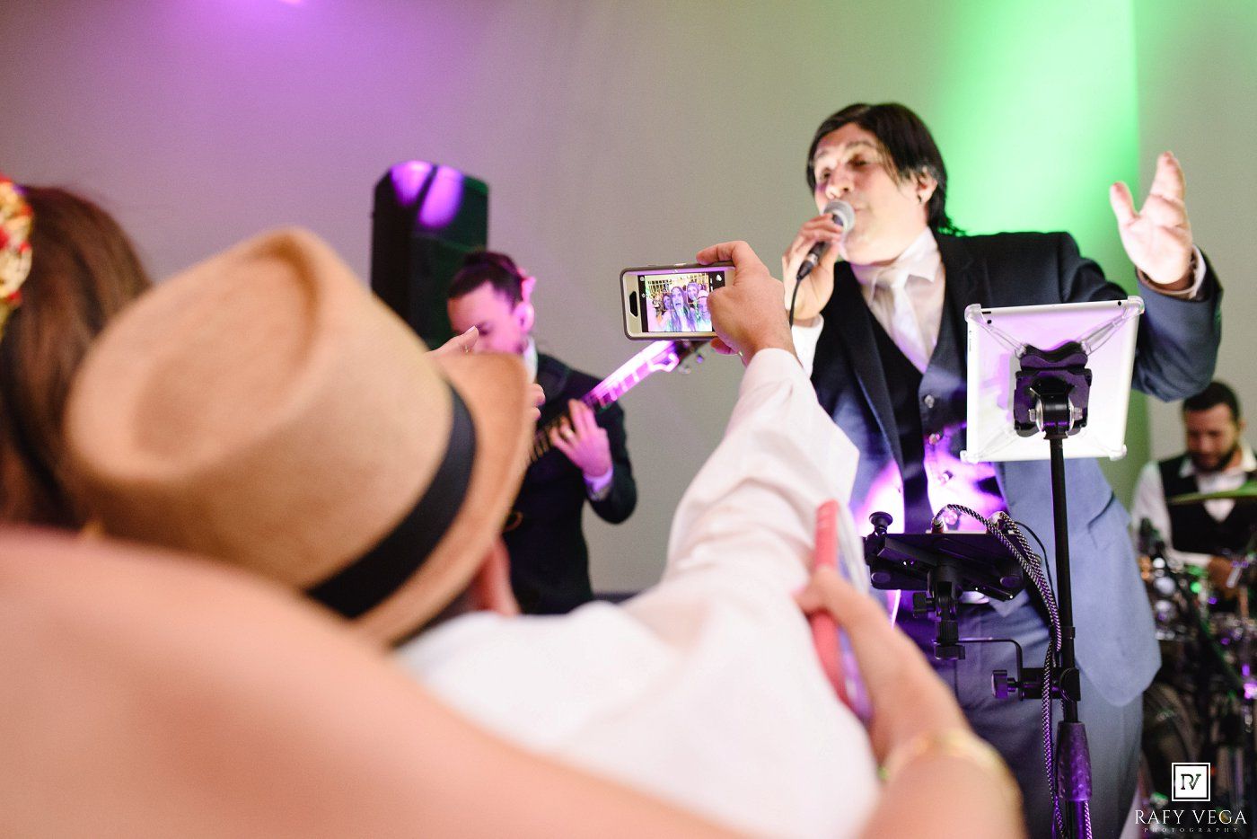 A performer sings into a microphone on stage while audience members record with smartphones at a lively event.