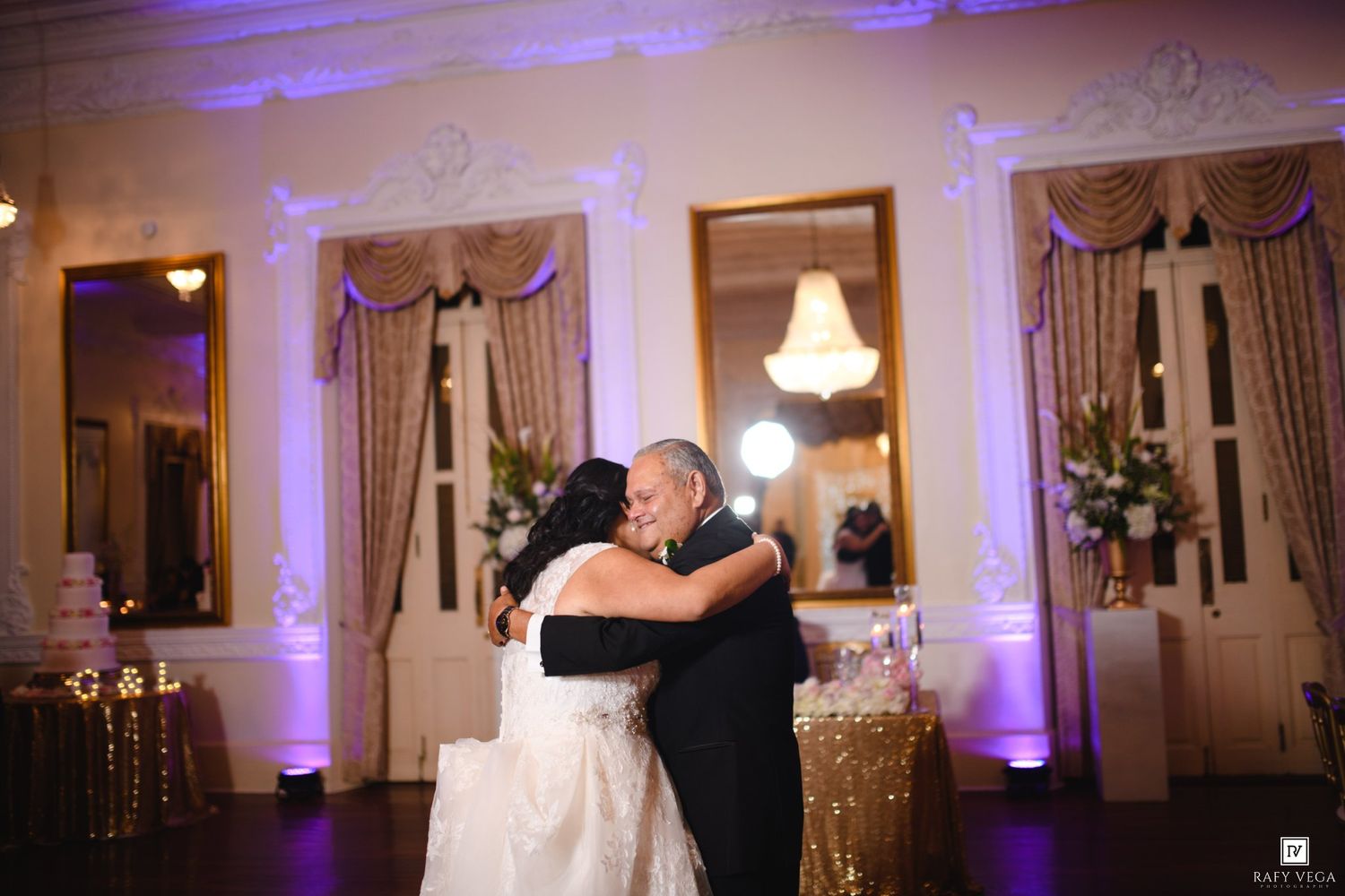 Bride and groom share an emotional first dance embrace in an elegant ballroom with purple uplighting.